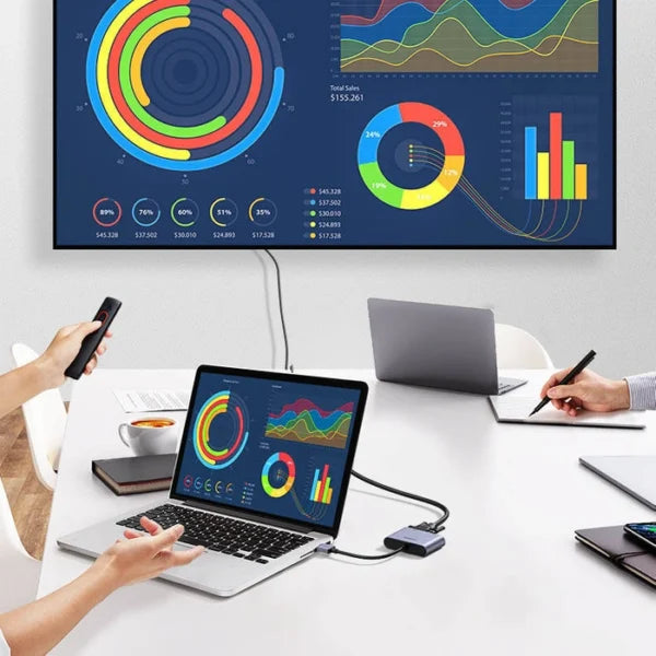 Two people working at a desk with laptops and a large screen displaying colorful graphs and charts.