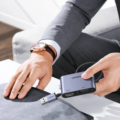 Person holding a Ugreen USB hub with multiple ports on a desk.