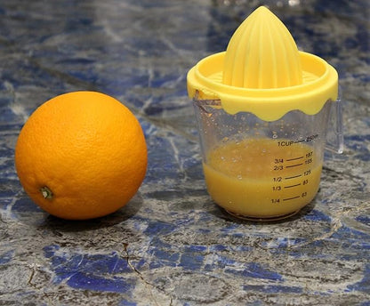 Yellow manual juicer with orange juice next to an orange on a blue marble surface