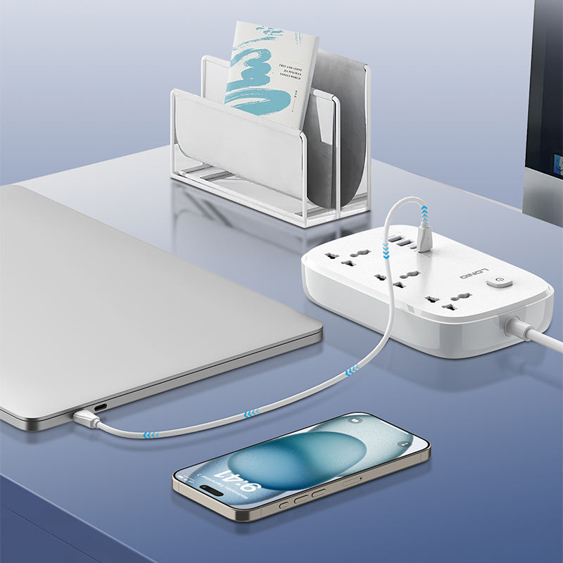 White power strip with multiple outlets and USB ports on a blue surface, with a smartphone and laptop in the foreground.