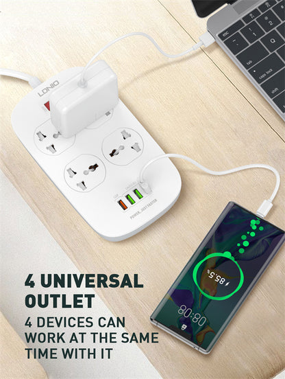 White power strip with multiple outlets and USB ports on a wooden surface, with a smartphone and laptop in the background.