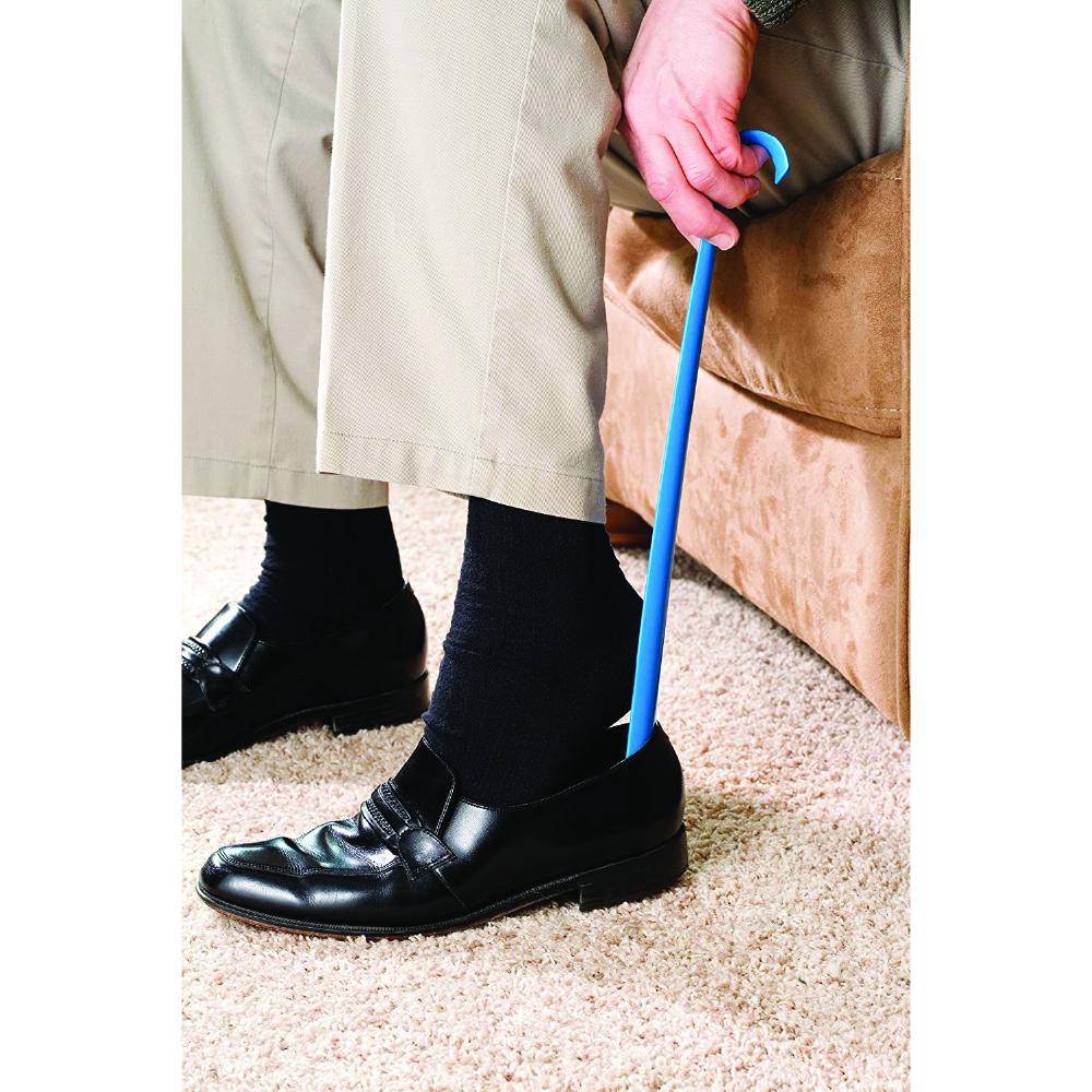 Person wearing black shoes and beige pants, holding a blue cane on a carpeted floor.