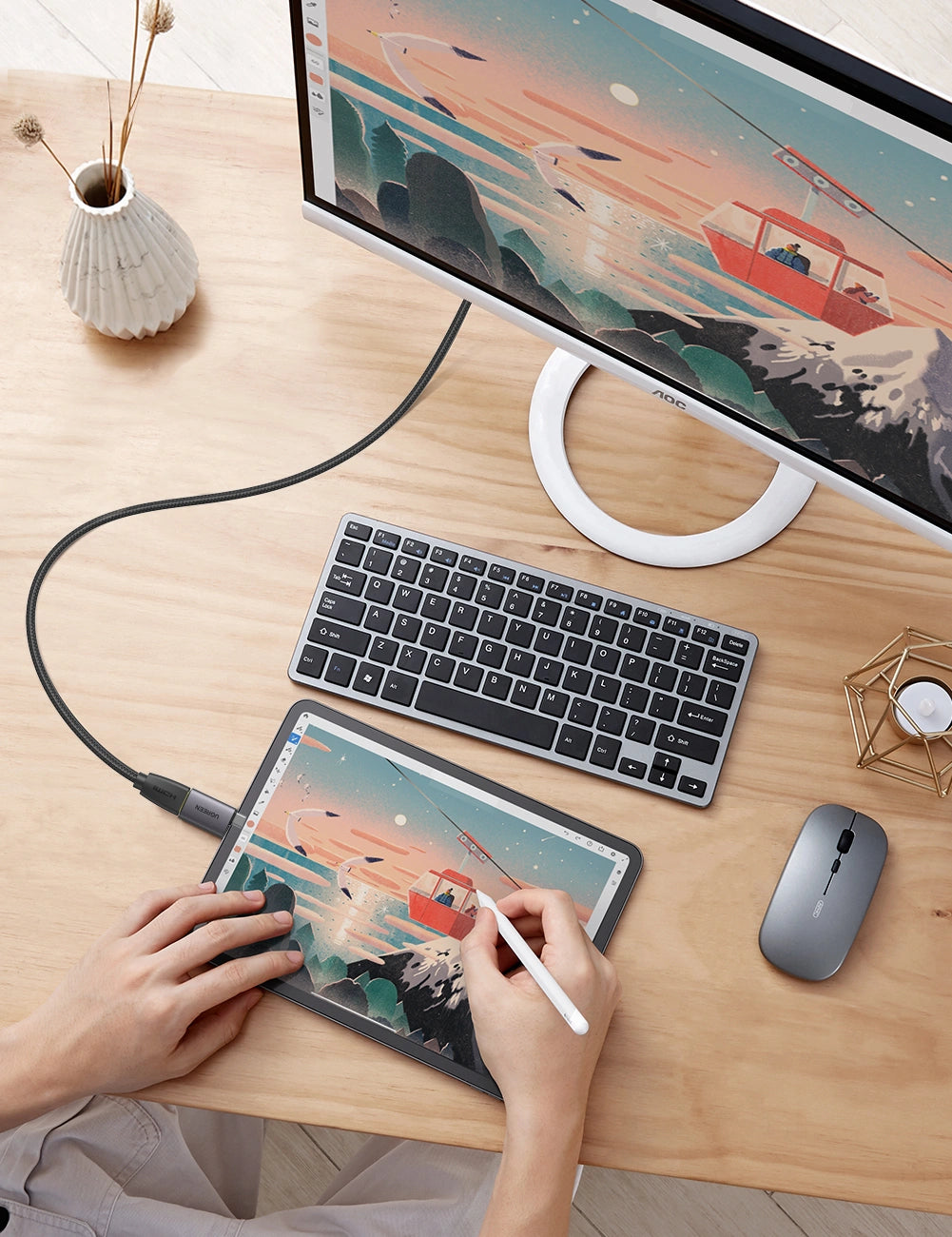 Person using a stylus on a digital drawing pad with a computer setup on a desk.
